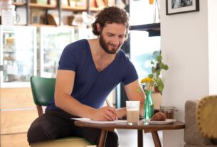 Smiling young man sitting in a coffee shop writing letter